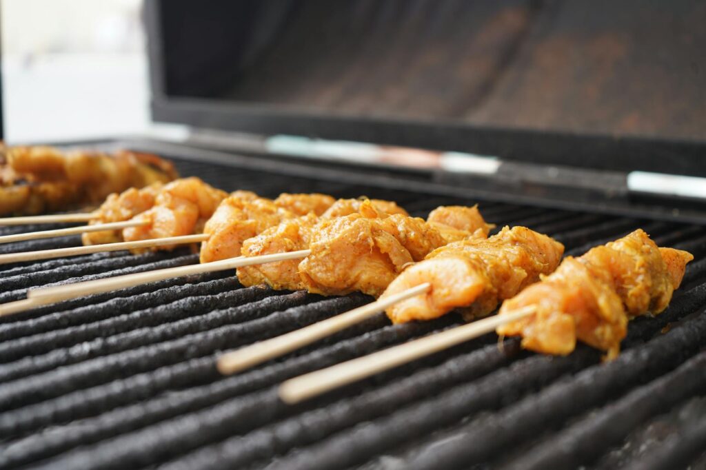 Barbecue électrique posé sur une terrasse en bois avec grillades de légumes et viandes