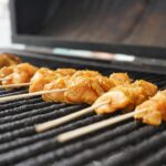 Barbecue électrique posé sur une terrasse en bois avec grillades de légumes et viandes