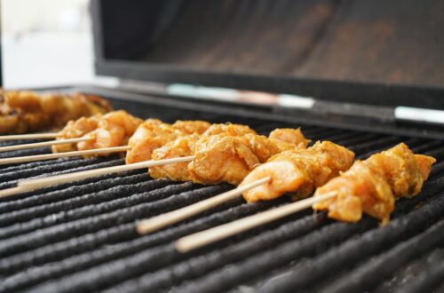 Barbecue électrique posé sur une terrasse en bois avec grillades de légumes et viandes